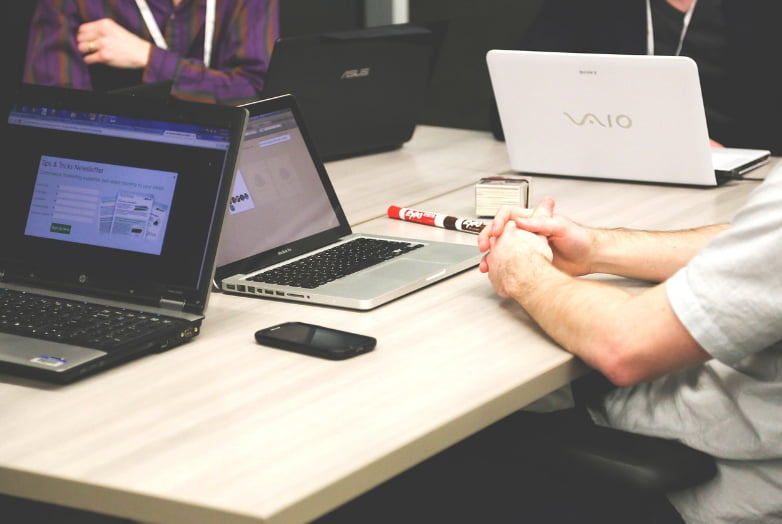 A man seated at a table, working on two laptops positioned in front of him.