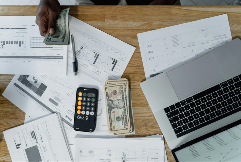 Businessman's hands on a desk with a laptop and scattered money, indicating a financial transaction or planning.