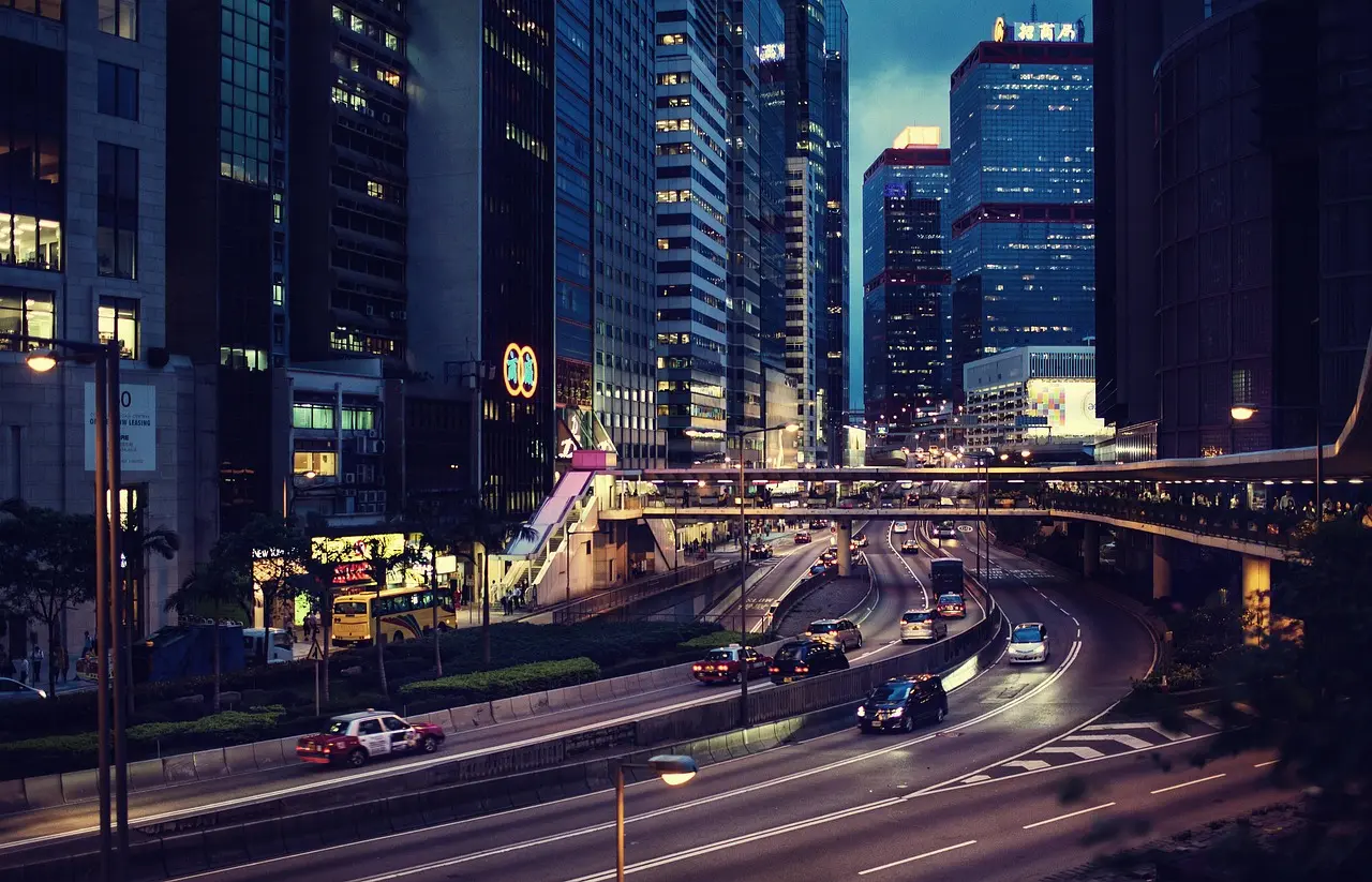 A bustling city street lined with buildings, featuring parked and moving cars under a clear blue sky.