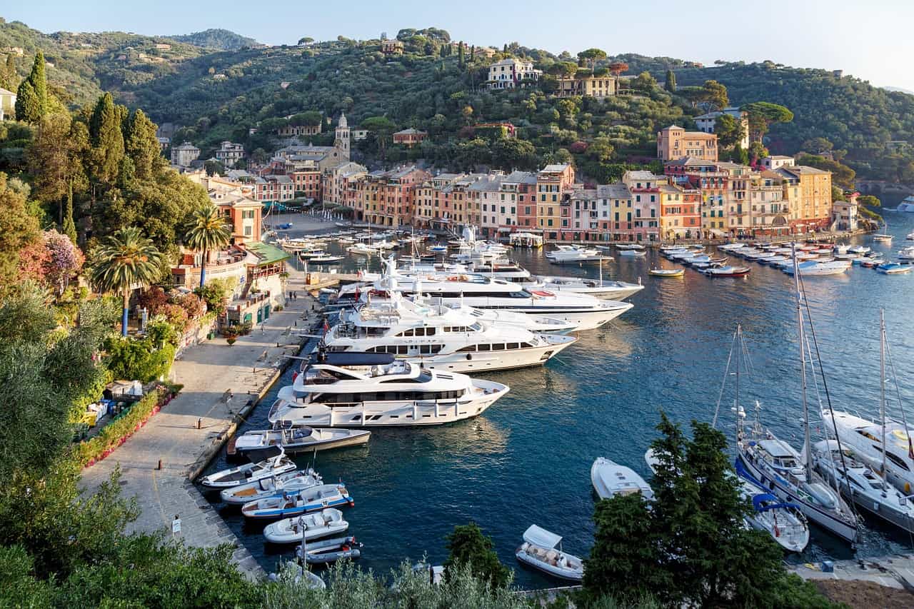 A picturesque landscape of Portofino, Italy, featuring vibrant waterfront buildings, boats, and surrounding hills under a clear sky.
