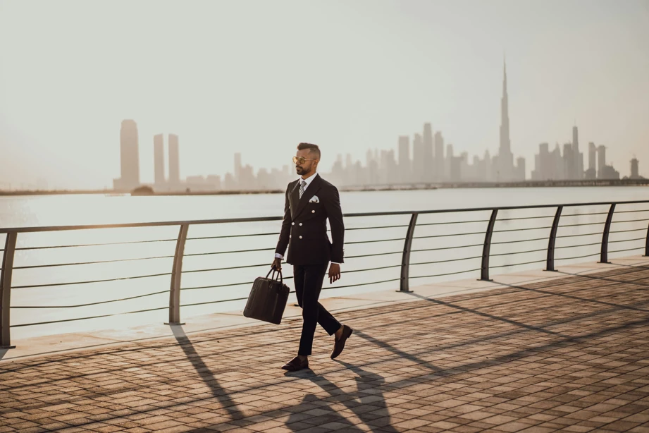 A man in a suit walks along a boardwalk, carrying a briefcase in his right hand.